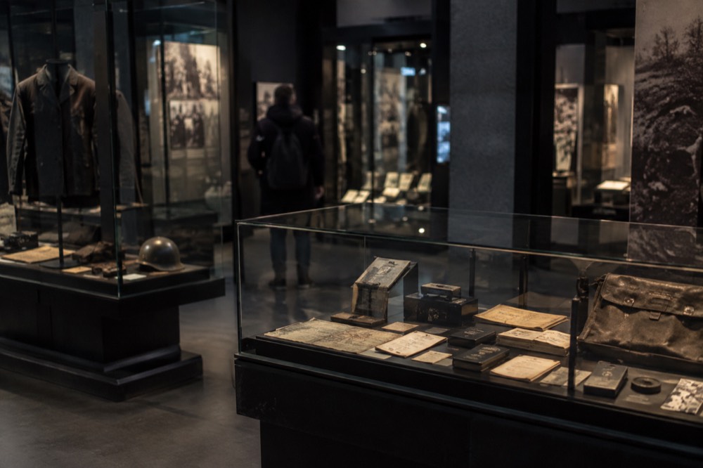 A dimly lit museum gallery with glass cases displaying wartime documents and artifacts