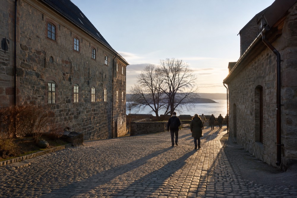 Visitors walking a cobblestone lane between stone buildings inside Akershus Fortress