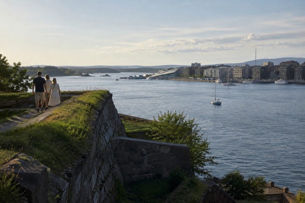 A stone rampart walk overlooking harbor water, boats and modern buildings across the bay