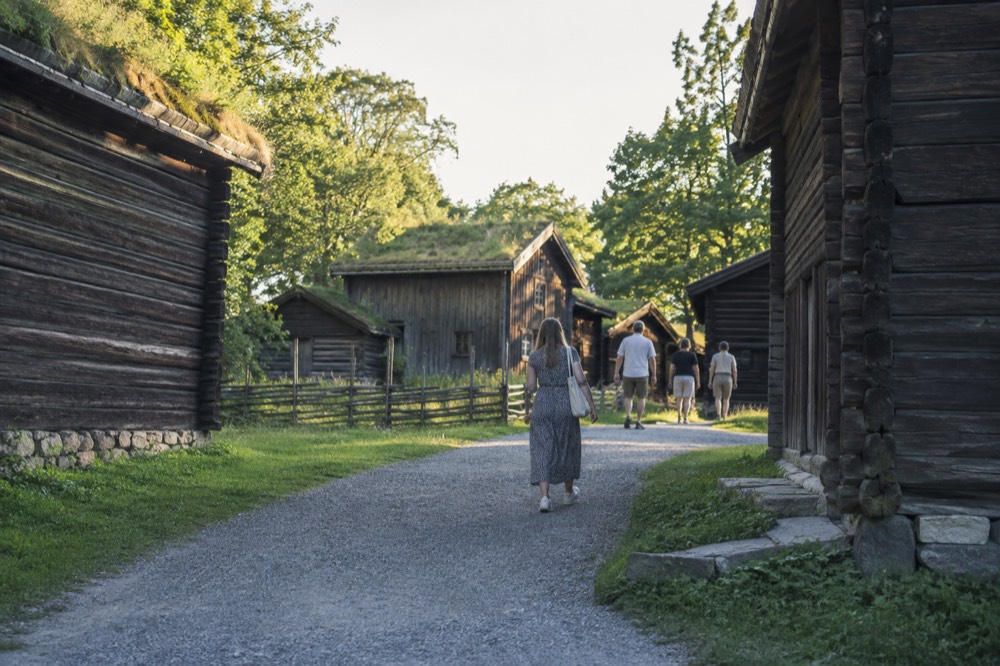 Visitors walking a gravel path between wooden farm buildings on a summer day