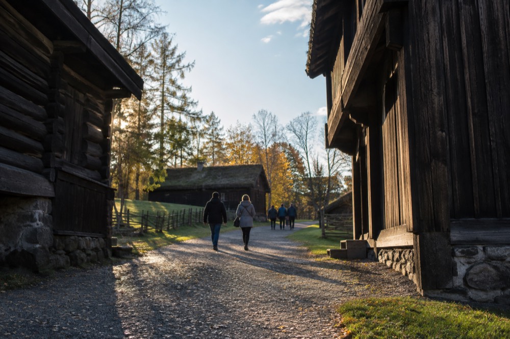 Gravel lane between wooden buildings with visitors walking in late afternoon light