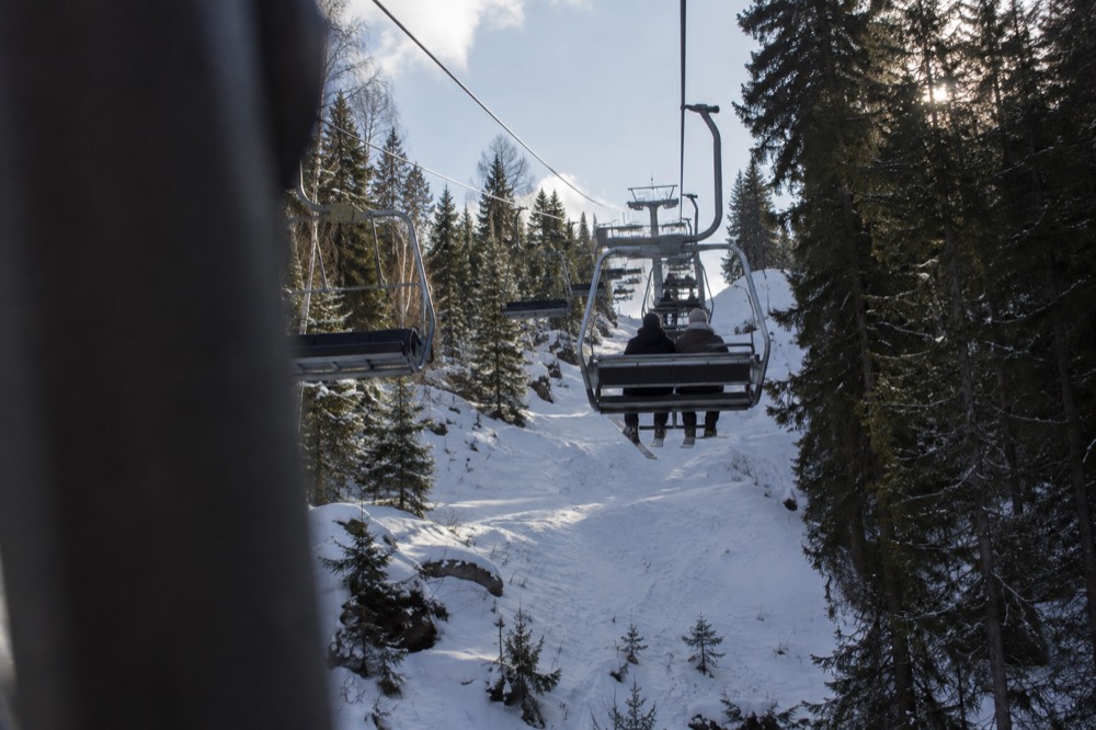 Chairlift carrying skiers up a snowy slope with pine forest on both sides