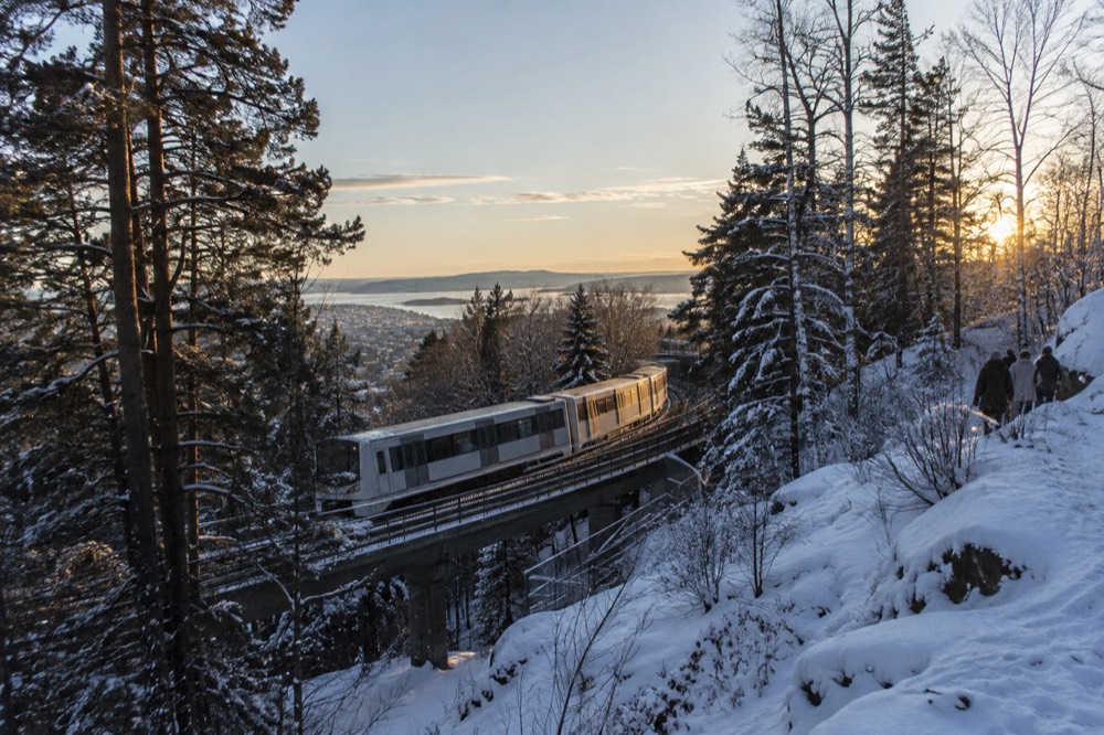 A metro train on an elevated track climbing through snow-dusted pine forest