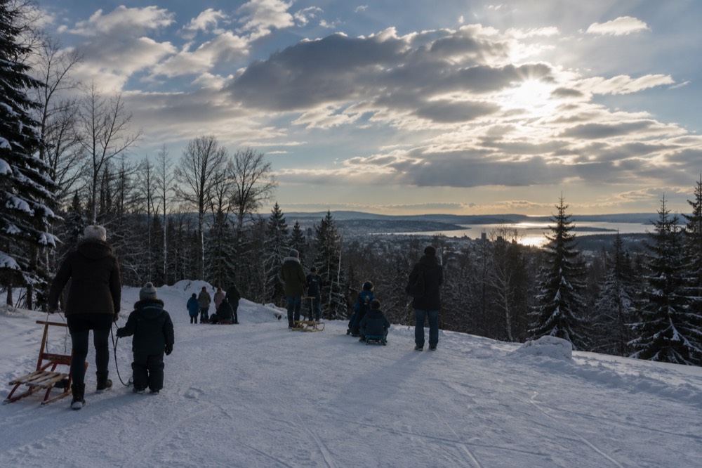 Sleds and families gathered at a snowy trailhead above the city
