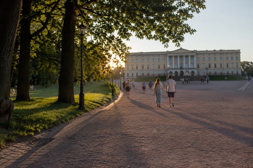 Visitors walking the gravel path toward the Royal Palace facade in Oslo on a summer evening