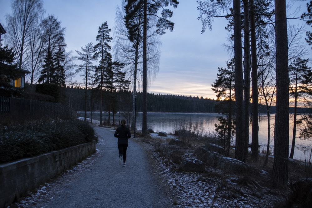 A gravel trail leading from a residential street toward a forested lake shoreline
