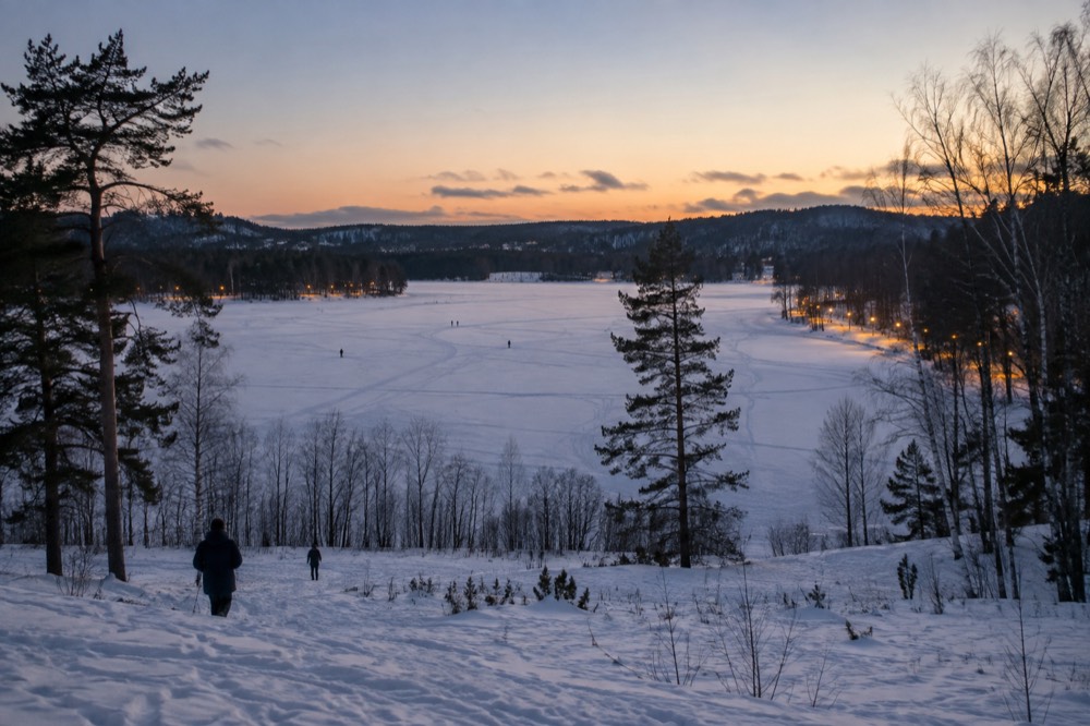 A frozen lake at dusk with lit ski trails glowing along the shoreline