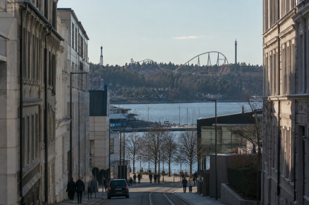Roller coaster track looping over a forested hillside beside a fjord inlet