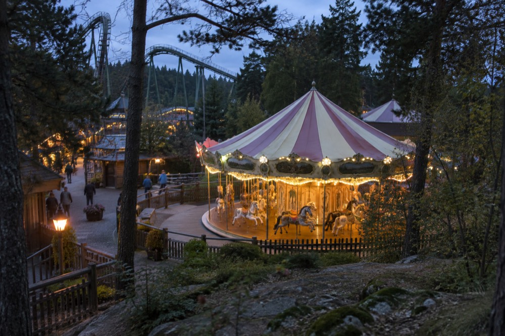 A children's carousel with painted horses under trees in an amusement park