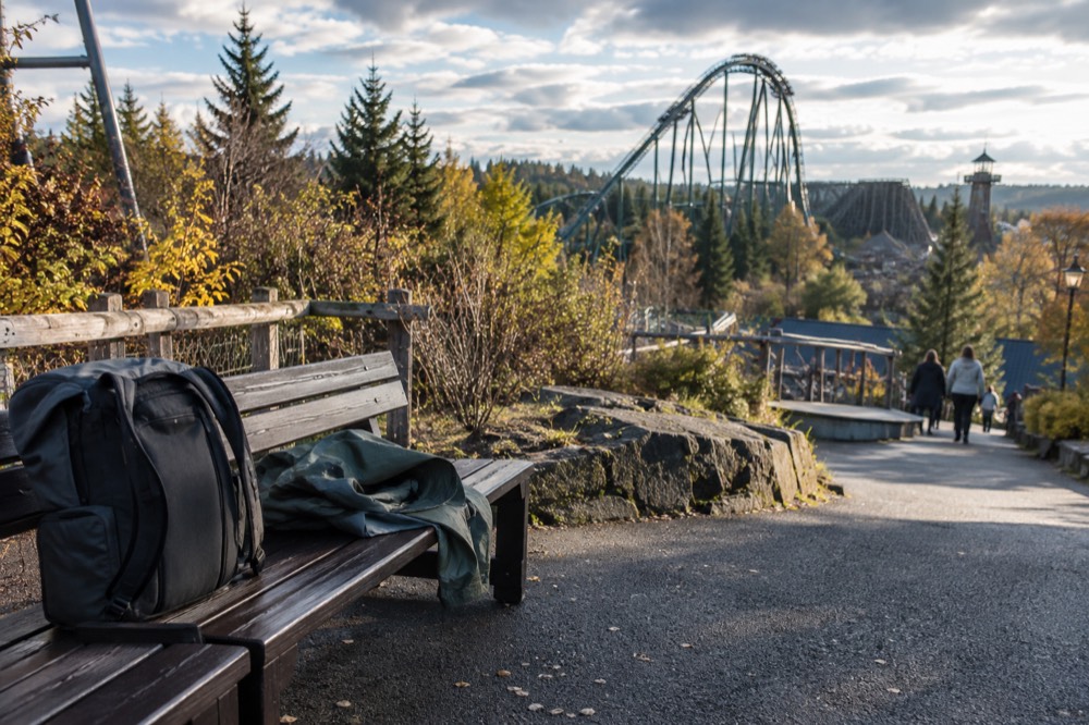 A backpack and folded rain jacket on a bench beside a park pathway