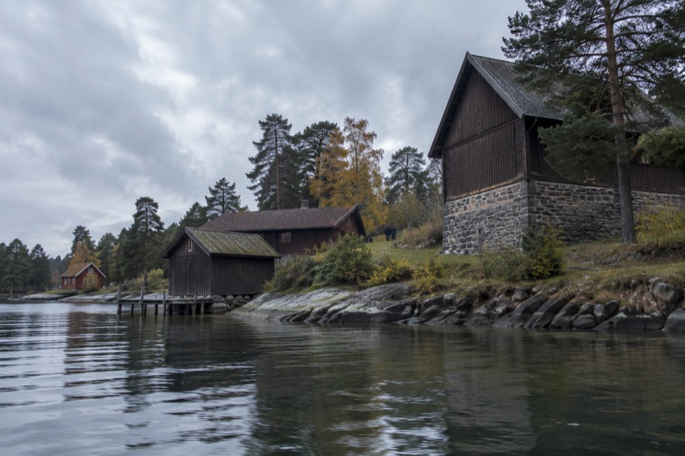 Wooden museum buildings on a green peninsula with calm water in the foreground