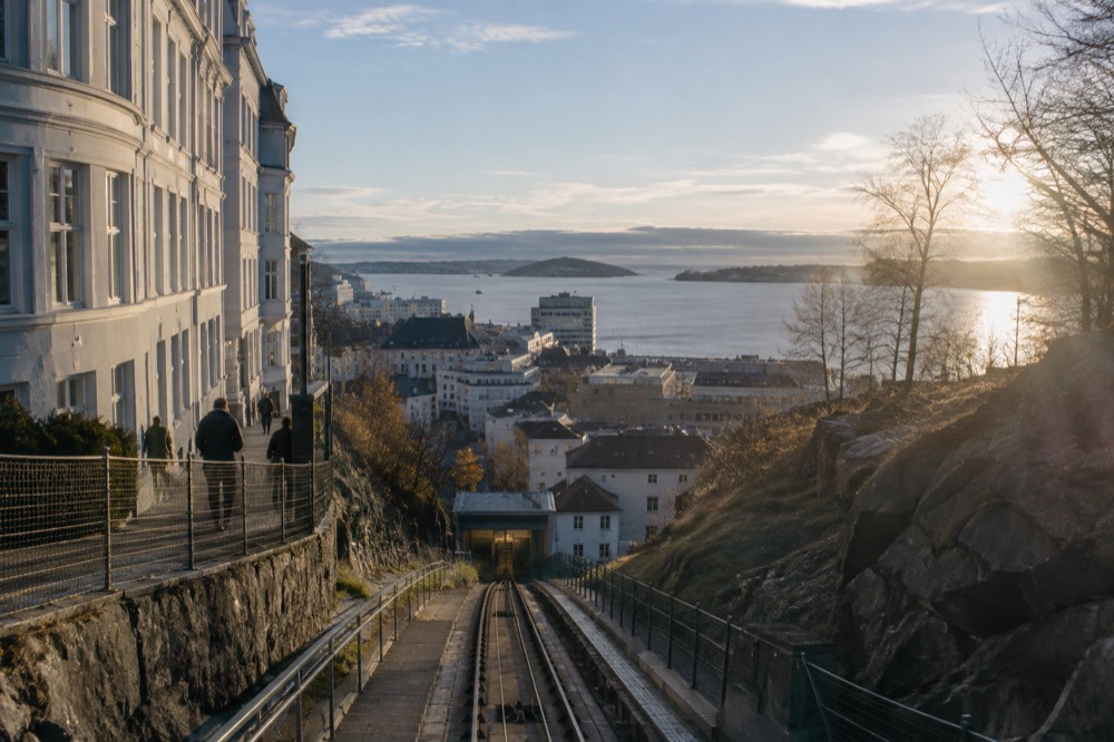 Steep mountain railway line descending toward a fjord village between cliffs