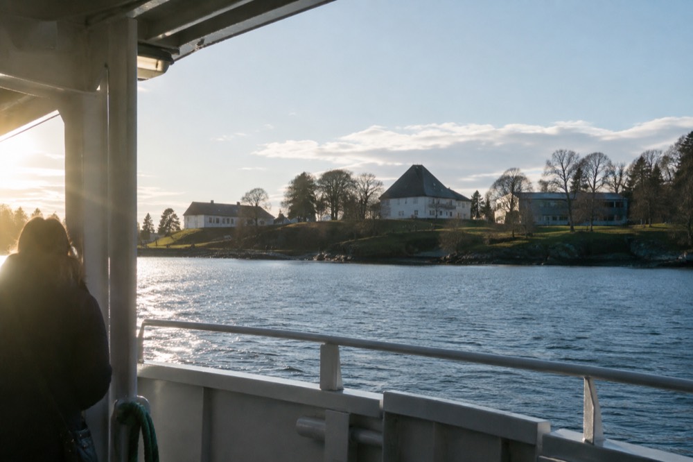 Museum buildings on a green peninsula seen across water from a ferry