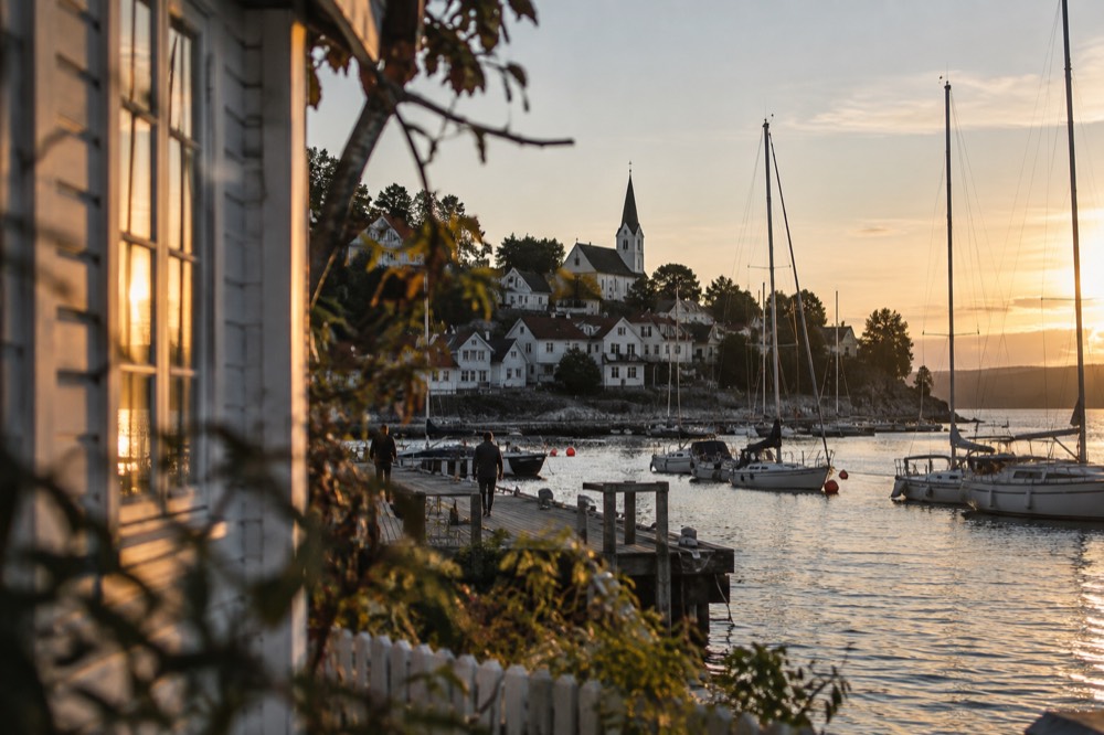 White wooden houses and a church above a small harbor with moored sailboats