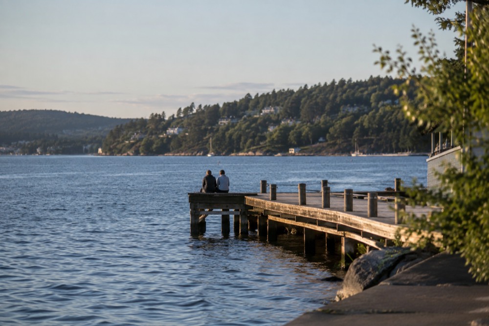 A wooden jetty extending into calm fjord water in evening light with forested shore behind