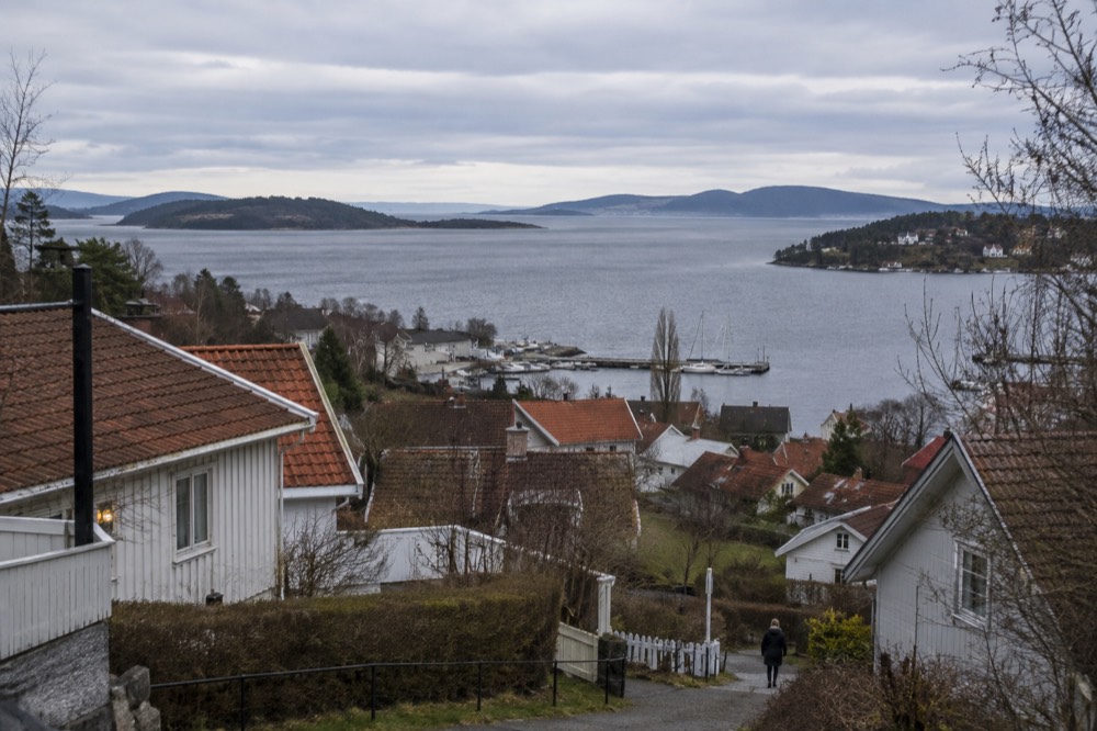 A view from a hillside over red rooftops and fjord water toward distant islands