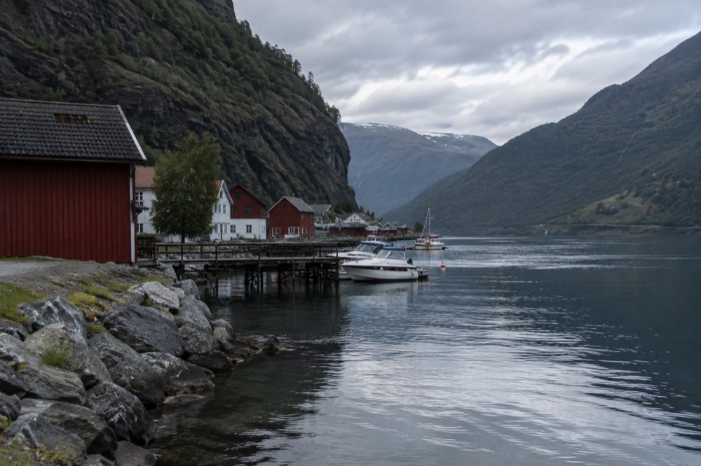 A small village of red and white buildings at the water's edge surrounded by steep forested cliffs