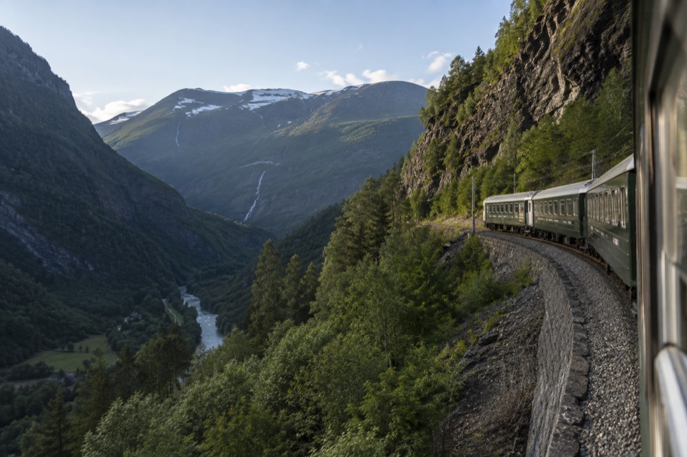 A passenger train on a mountain line curving along a rock ledge above a valley