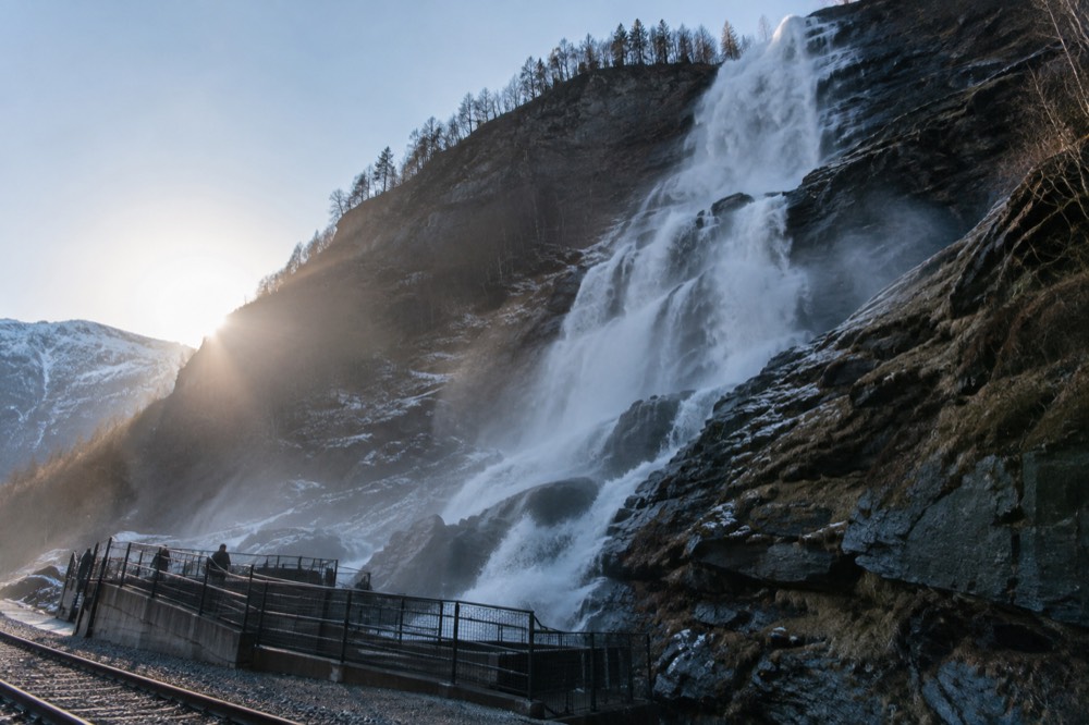 A large waterfall pouring down a rock face beside a railway viewing platform