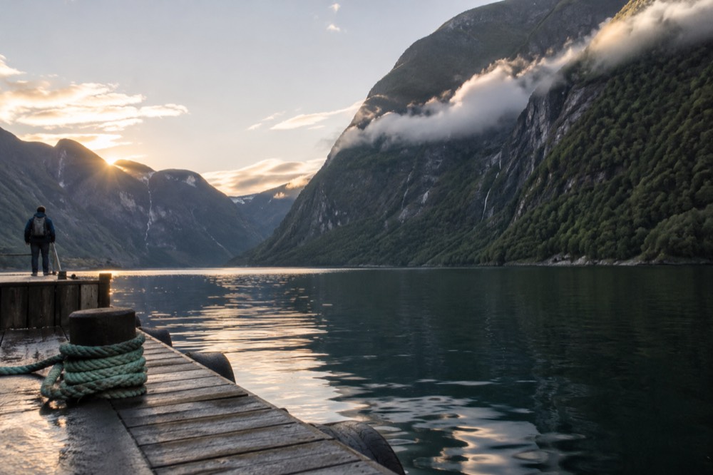 A narrow fjord with calm dark water and steep forested walls under low clouds