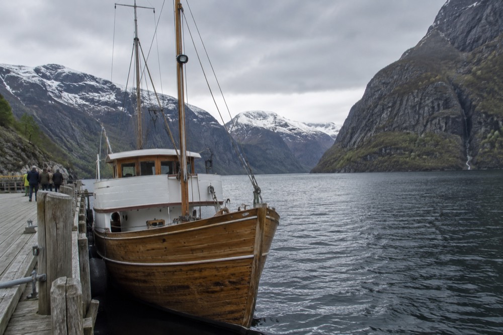 A wooden sightseeing boat moored at a small pier on a narrow fjord