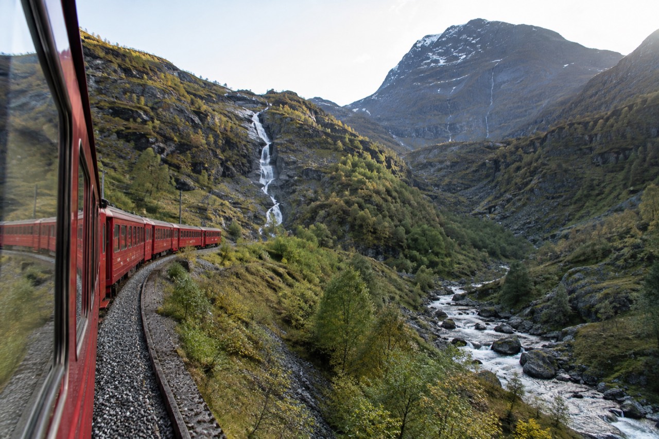 A red railway carriage climbing steep green mountains beside a waterfall in western Norway