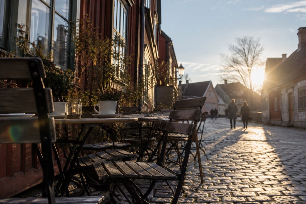 Cafe tables with coffee cups set out on a cobblestone street beside old timber facades