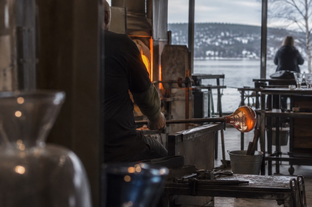 A glassblower shaping a glowing bubble of molten glass on the end of a steel pipe