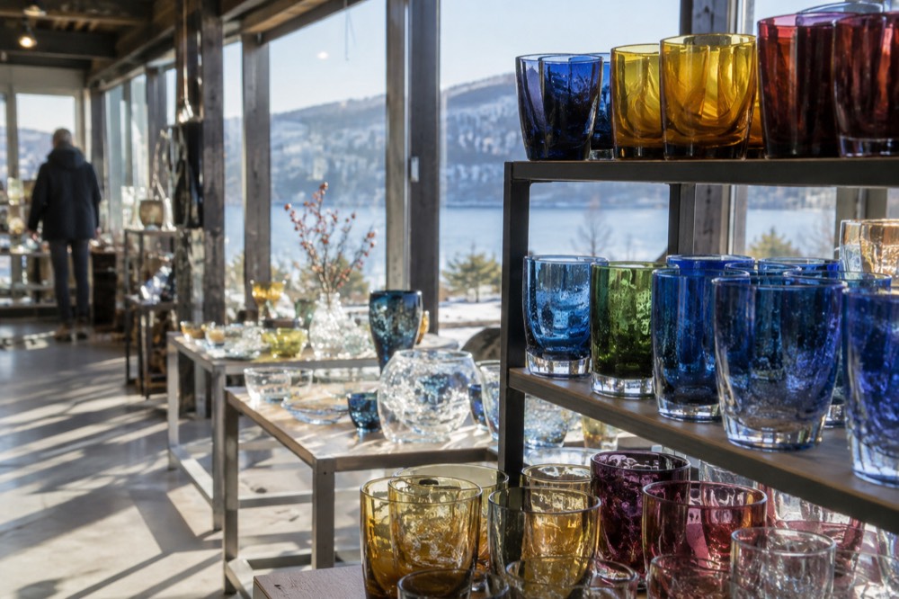 Shelves of hand-blown drinking glasses in bright colors inside a glassworks outlet shop