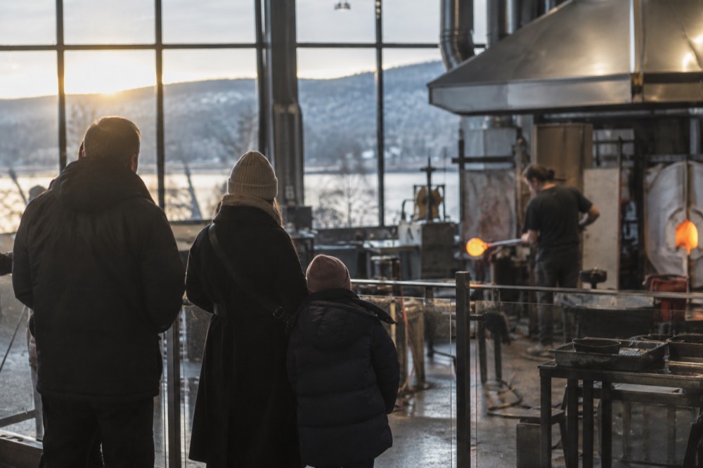 A family watching a glassblower work behind a safety barrier in a bright workshop