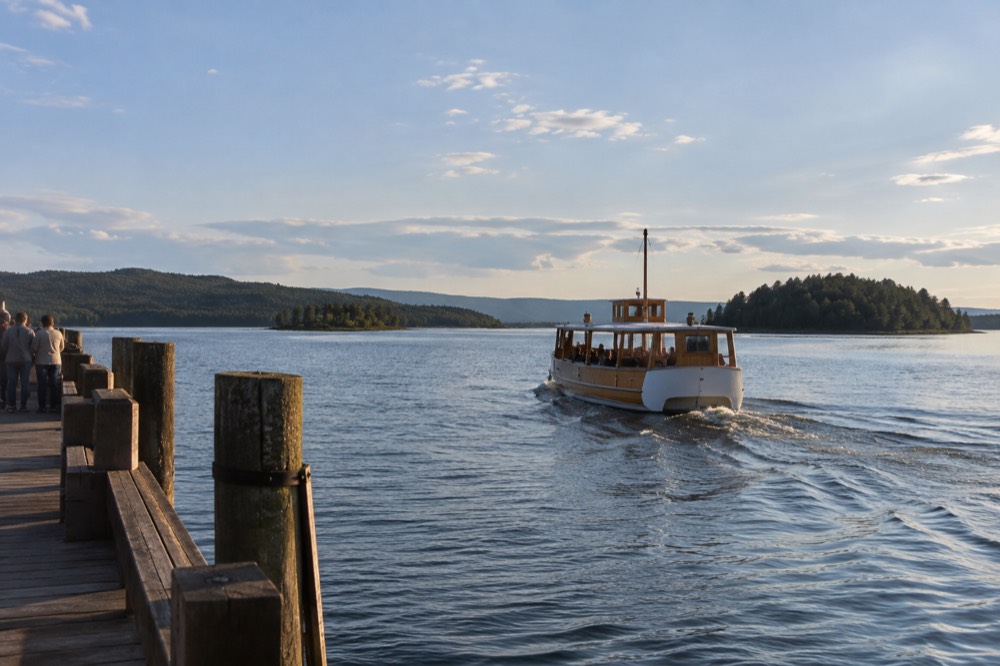 A wooden ferry departing a city pier toward green islands in a calm fjord