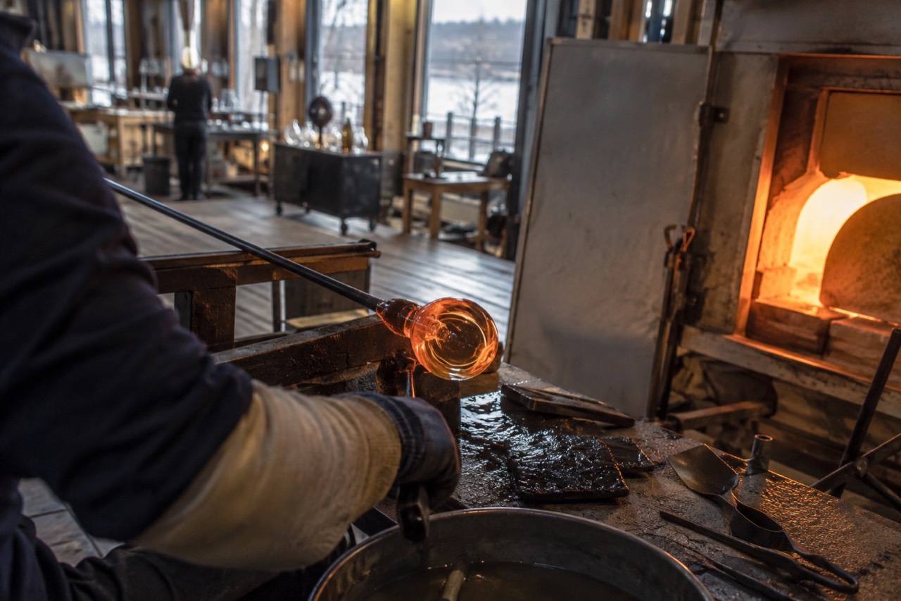 Glowing molten glass being shaped on a blowpipe inside a glassworks hot shop