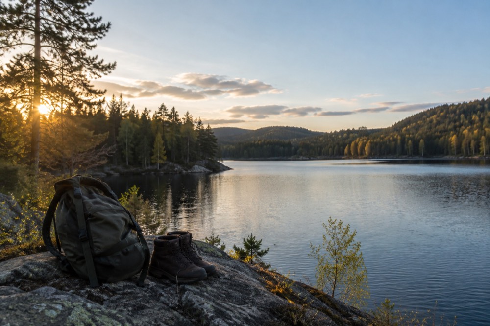 Backpack and hiking boots on a rock beside a forest lake