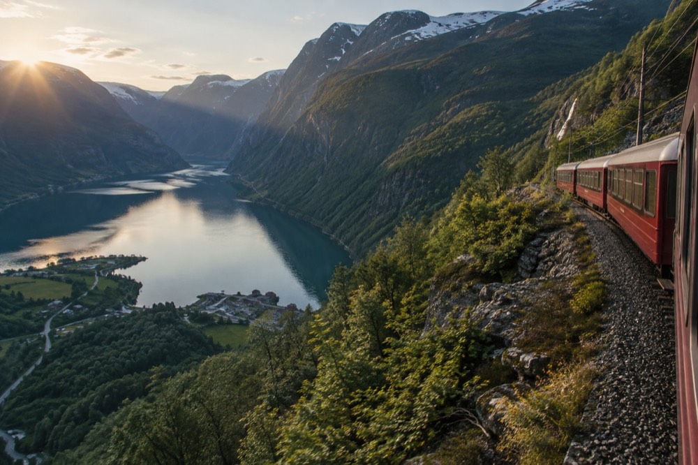 A red railway carriage on a steep mountainside line above a deep green fjord