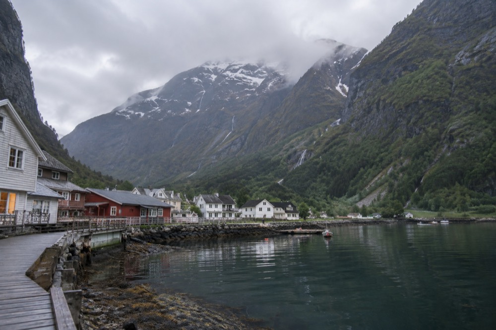 A small fjord village of wooden houses at the water's edge beneath steep cliffs