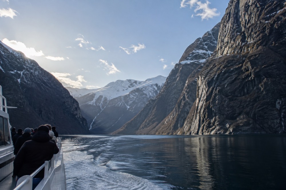 A sightseeing boat moving through a narrow fjord with sheer rock walls on both sides