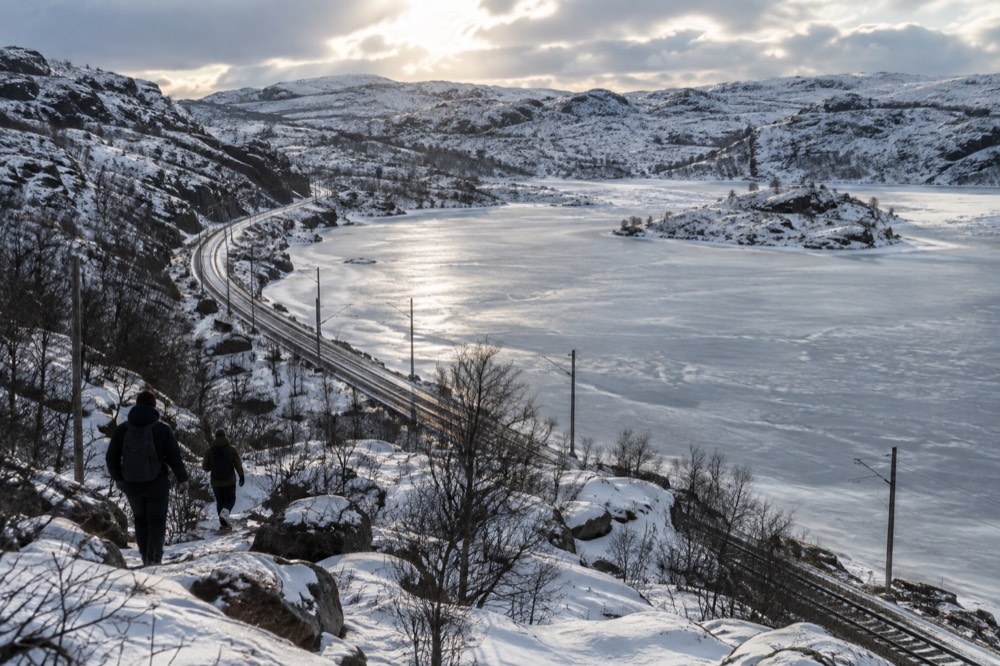 A mountain plateau with a rail line running beside a frozen lake under a low sky