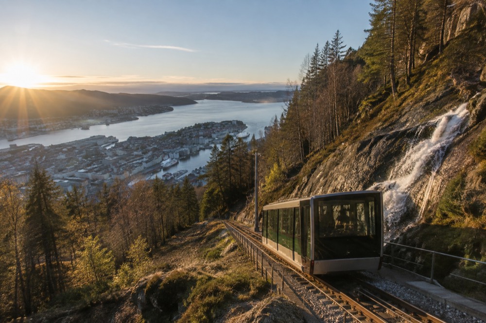 A steep mountain railway descending past waterfalls toward a narrow fjord