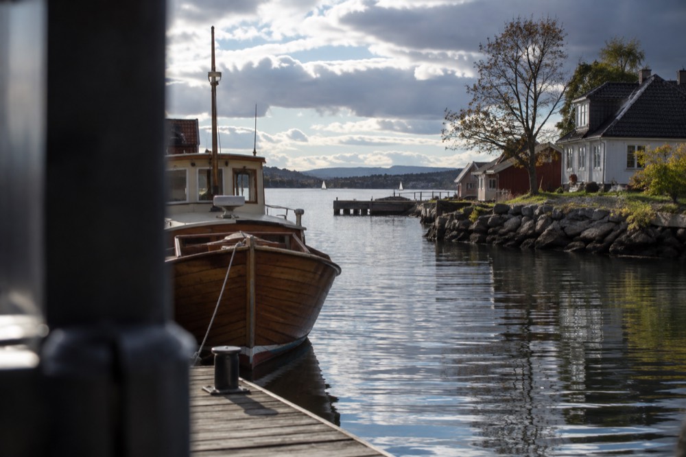 A wooden fjord boat moored beside a small village at the end of a narrow waterway