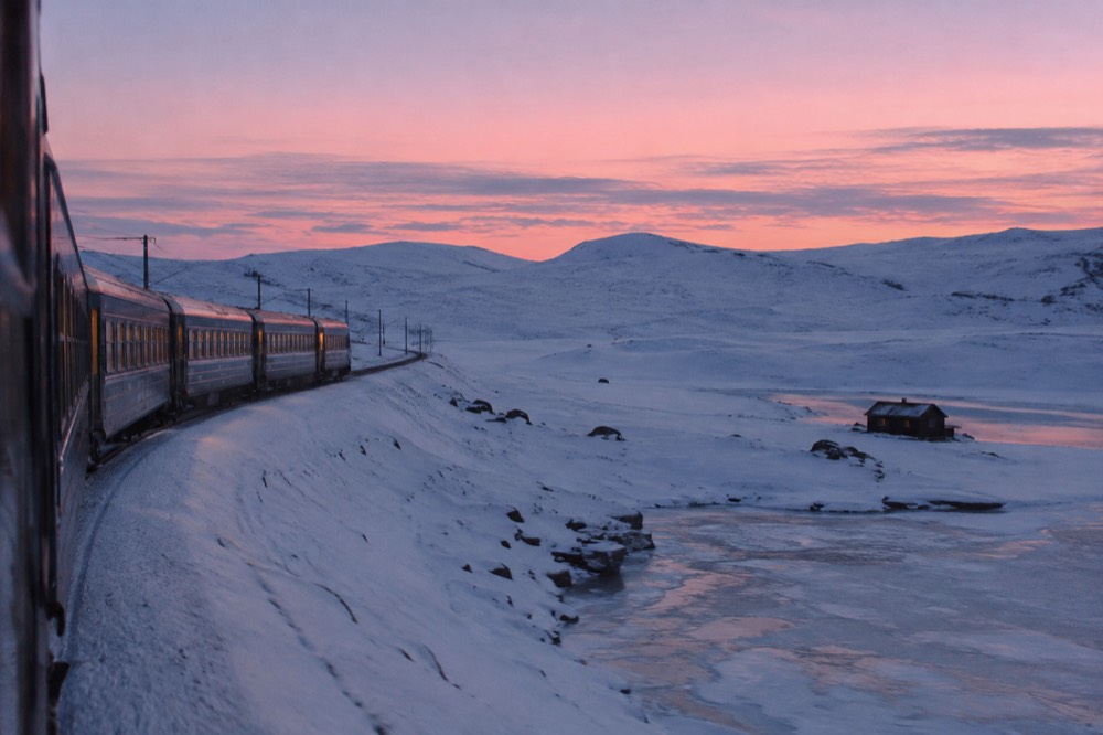 A train crossing an endless snow plateau under a pink winter sky at dusk