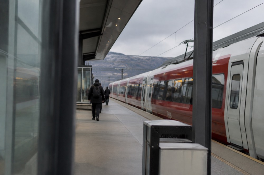 A modern airport train platform with a red and white train waiting beside a terminal building
