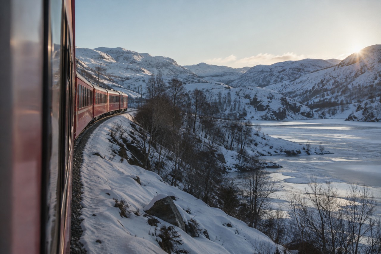 A red train winding through snow-covered mountains above a frozen lake in central Norway
