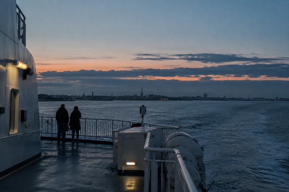 The stern of a large passenger ferry at dusk with deck railings and calm sea beyond