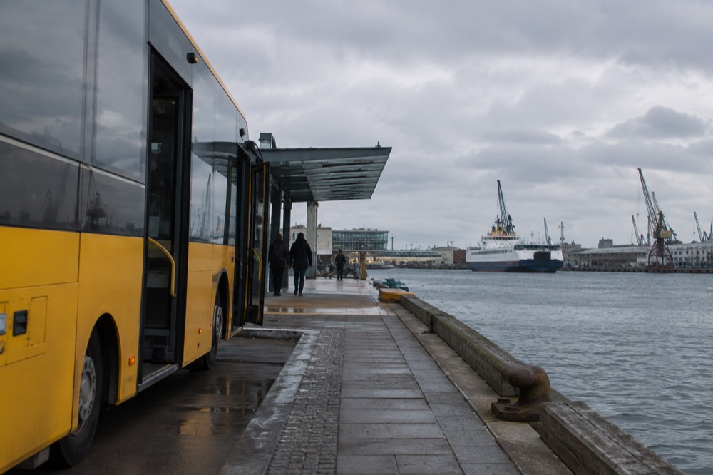 A city bus stopped at a waterside stop in Oslo with ferry cranes visible behind