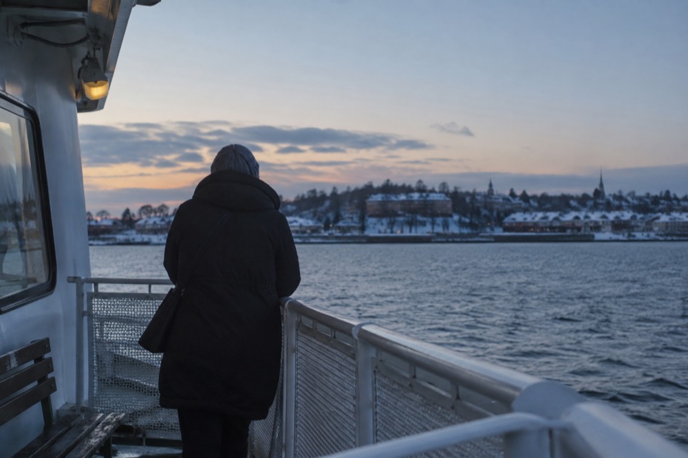 A ferry deck in winter with a passenger in a warm coat looking toward snow-dusted coastline