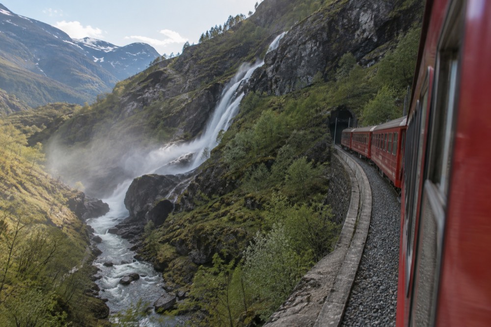 A red railway carriage on a steep mountain line curving beside a waterfall