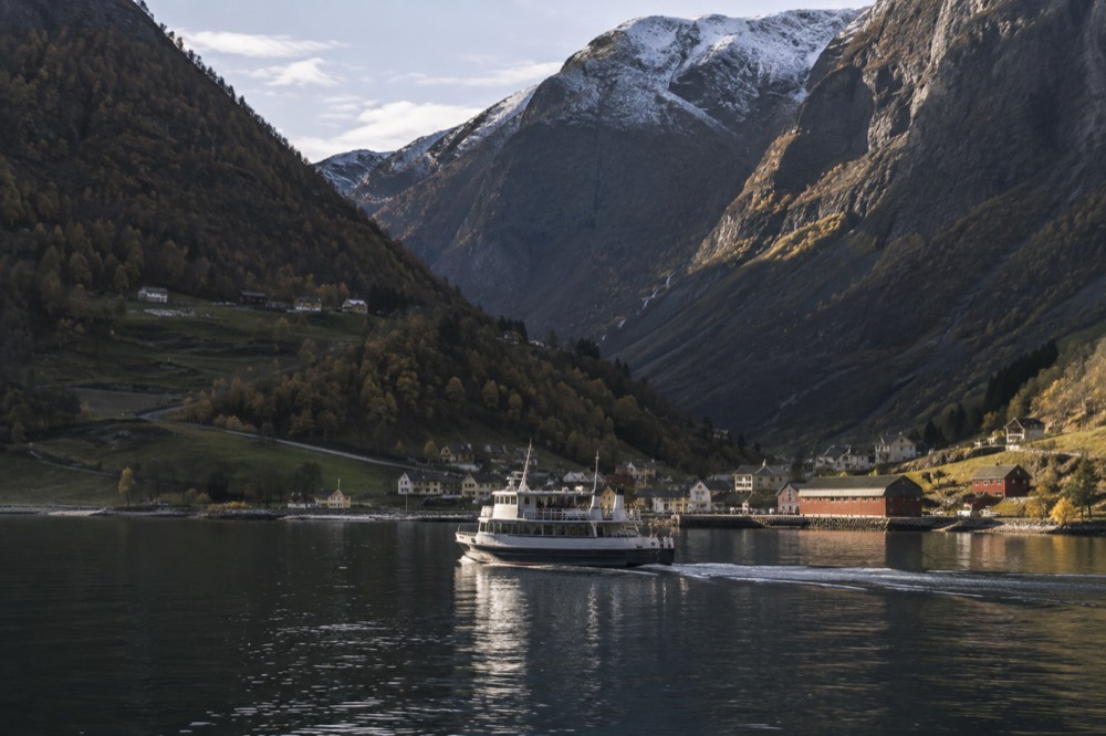 A cruise boat on calm dark water between two steep rock cliffs with a small village at the shore