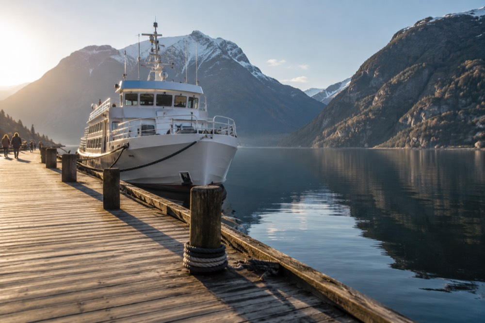 A wooden pier on a fjord with a white cruise boat tied up and mountains reflected in still water