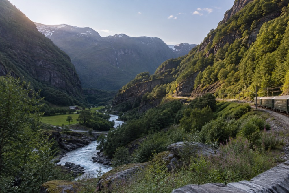 A steep green valley with a river running through it and a railway line cut into the hillside