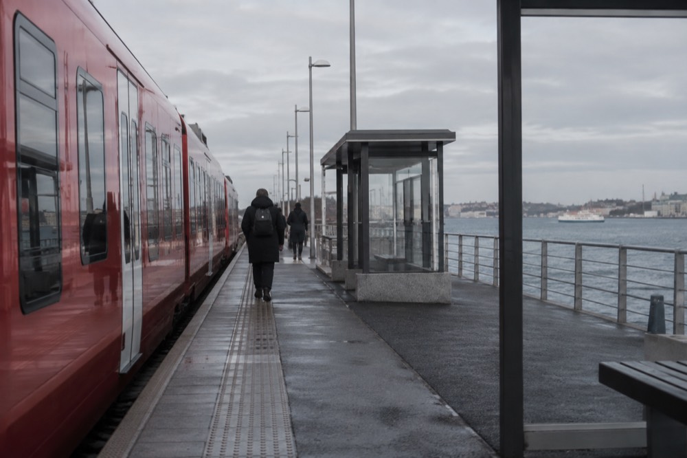 A red regional train stopped at a Swedish station platform beside the sea